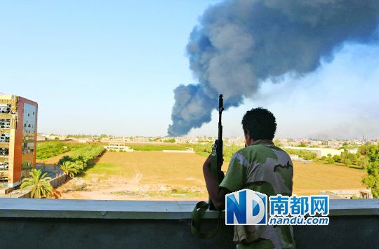 2日，利比亞首都的黎波里，一民兵武裝成員眺望被火箭彈擊中的儲(chǔ)油罐冒出濃煙。