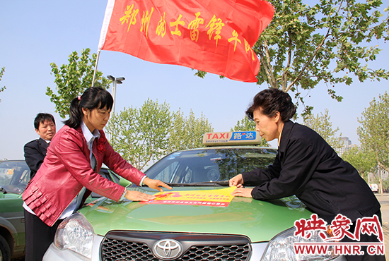 　　授旗結(jié)束后，首都的士雷鋒車隊(duì)王鳳進(jìn)隊(duì)長(zhǎng)（右）與鄭州的的哥的姐在車身上貼上標(biāo)識(shí)。