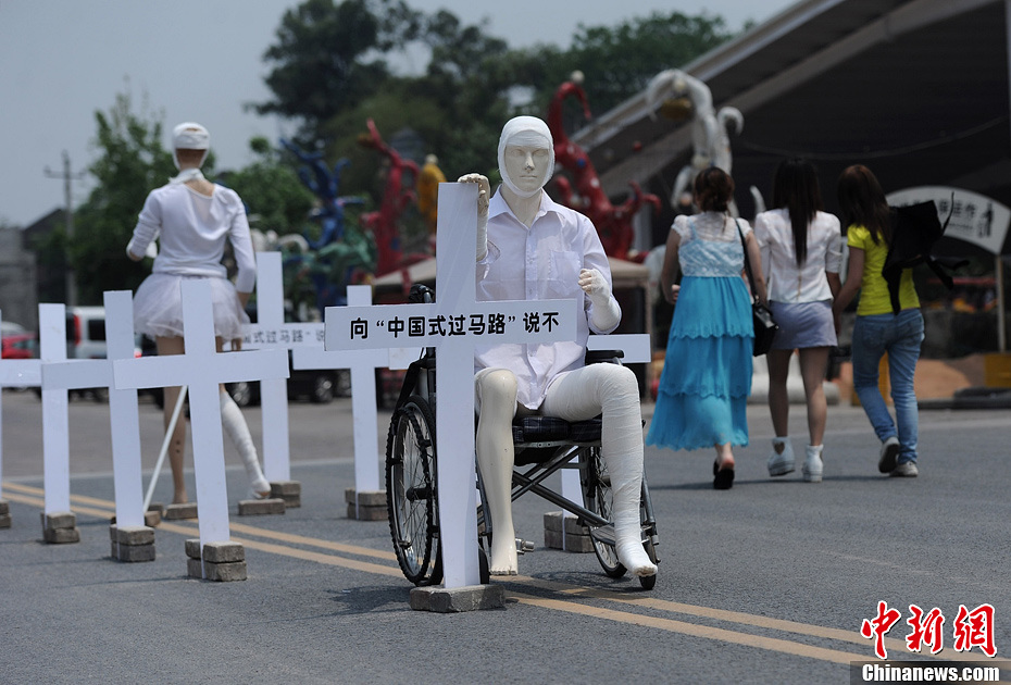 4月16日，重慶市洋人街上擺放著兩個(gè)受了傷的塑料人像“模特”，旁邊十字架上寫(xiě)著向“中國(guó)式過(guò)馬路”說(shuō)不