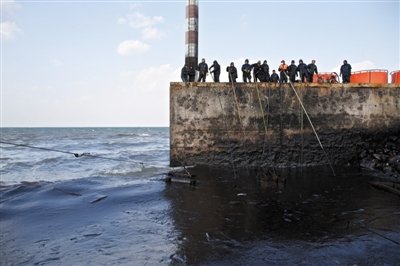 昨日，山東青島，清污人員正在海邊清理油污。