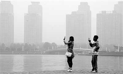 29日中午，鄭東新區(qū)如意湖畔，兩個年輕人拍攝霧霾中的景色。 鄭州晚報記者 馬健 圖