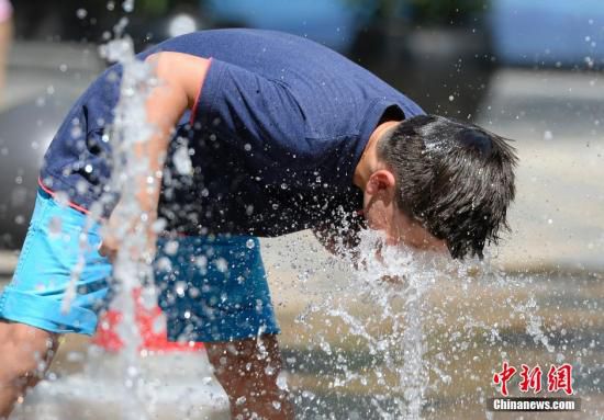 5月29日，一名小孩將頭伸向北京街頭的噴泉以降溫祛暑。