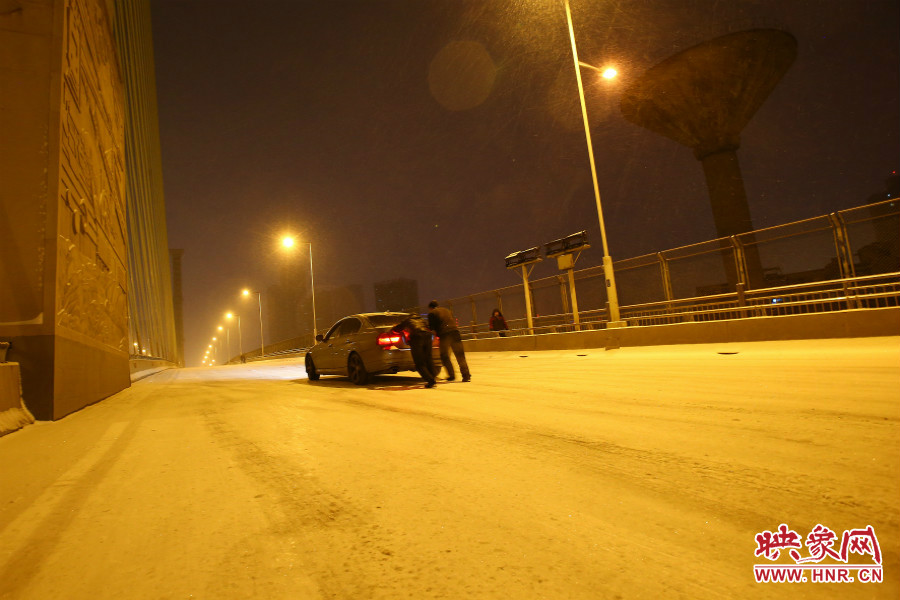 雪天路滑，汽車上橋打滑，兩名“推車人”幫助一輛私家車上坡。