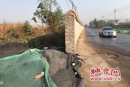 一墻之隔，一邊是道路，一邊是垃圾和荒草，市民質(zhì)疑其為遮羞墻。
