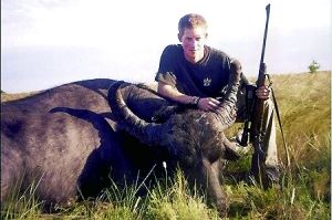 哈里王子手持獵槍，蹲在一頭遭到獵殺的水牛旁邊