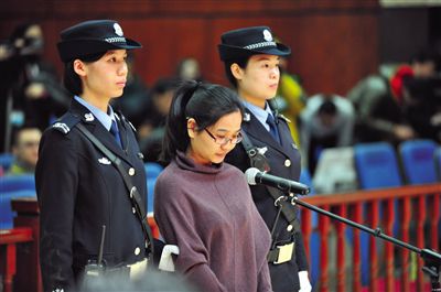 被告人盧梅低著頭，站在朝陽(yáng)法院刑事審判庭的被告席上。